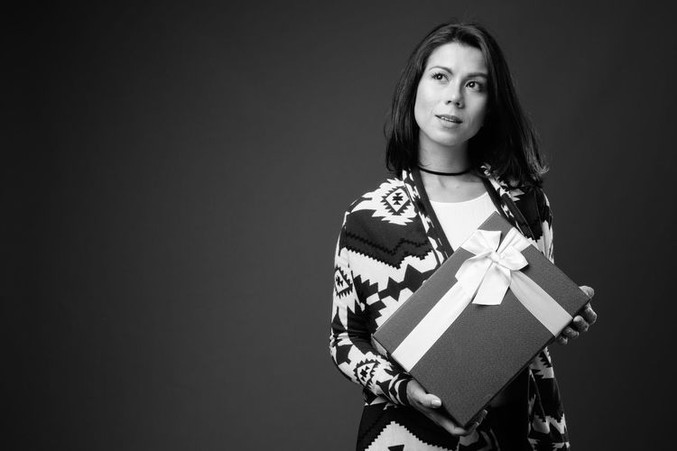 Woman looking away while holding gift box against black background