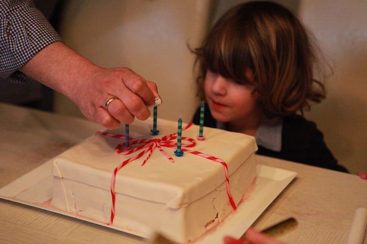 Cropped image of person with boy and birthday cake at table