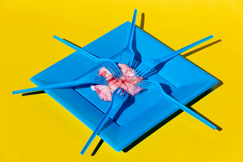 Heap of pink raw brains served on blue plate with plastic fork on yellow background in light modern creative studio