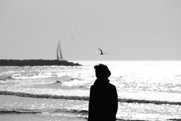 Rear view of man standing by sea against sky