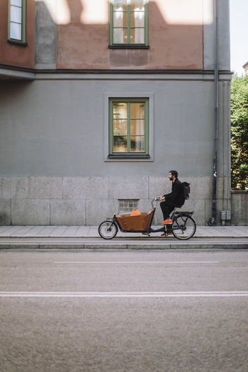 Businessman riding cargo bike on bicycle lane near building