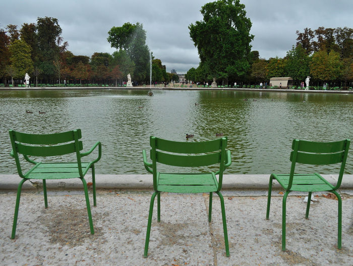 Empty chairs at lakeshore against sky