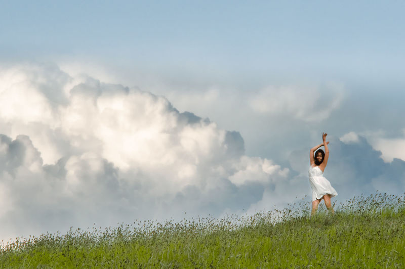 Runaway bride in a white dress dancing on the horizon on the background of a cumulus clouds