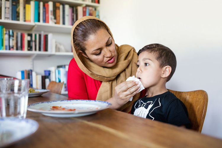 Mother wiping son's mouth after lunch at dining table