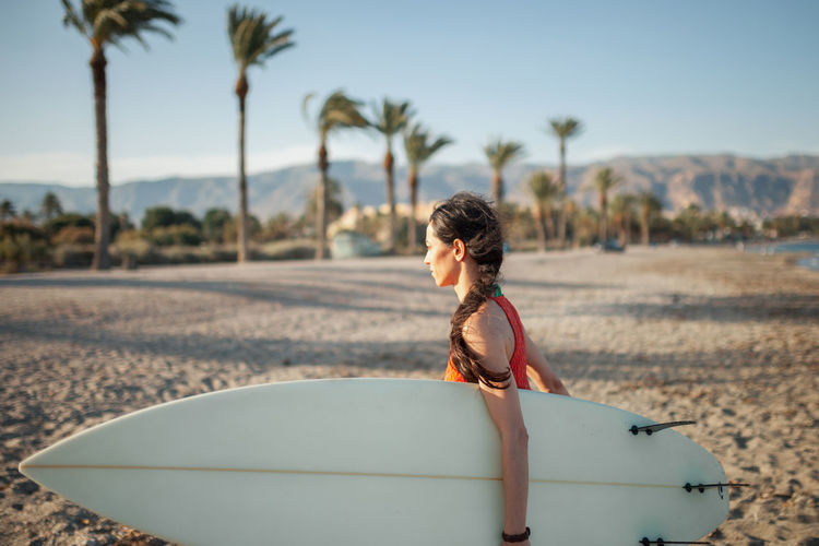 Side view of woman carrying surfboard while walking at beach