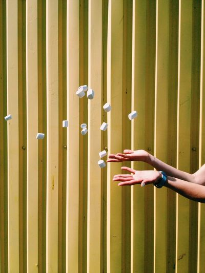 Cropped image of person throwing marshmallows against yellow wall