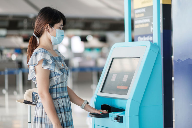 Side view of woman wearing mask standing by ticket machine