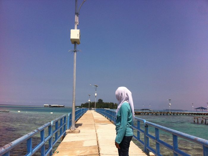 Side view of young woman standing on pier over sea against clear sky during sunny day