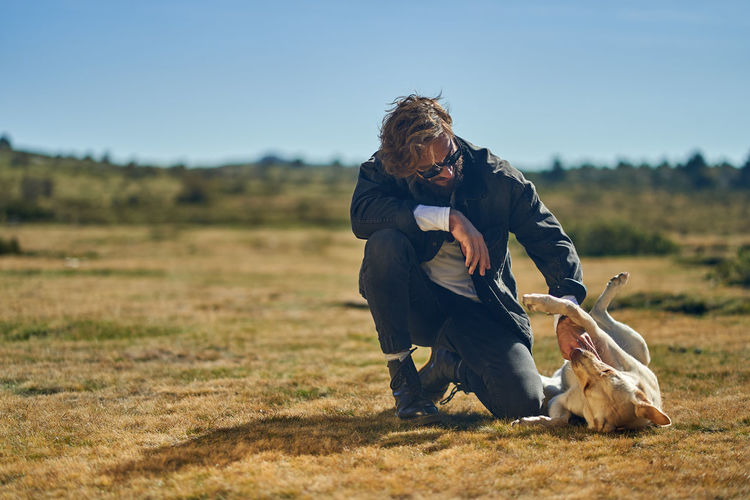 Portrait of young tattoed man playing with his dog in the countryside