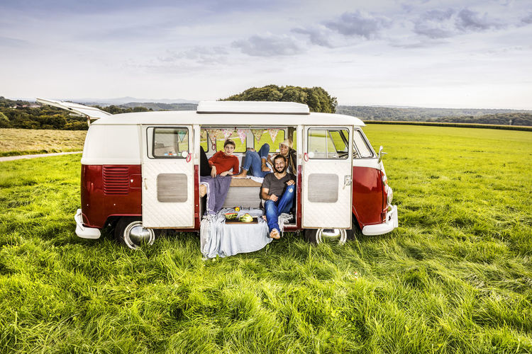 Friends having picnic in a van parked on field in rural landscape