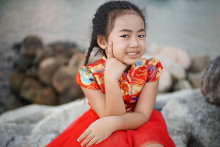 Portrait of smiling girl sitting on rocks against sea