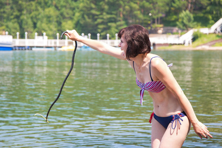 The woman was terribly scared of a water snake, holds it by the tail and screams in fear.