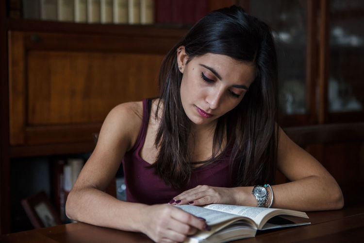 Concentrated young woman reading book at desk