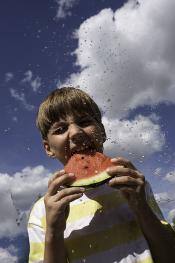 Portrait of boy with slice of watermelon against blue sky