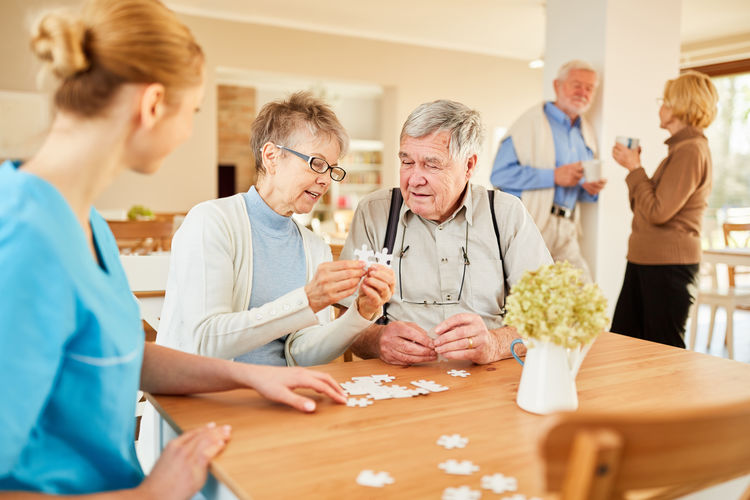 Smiling nurse with senior people playing with jigsaw puzzle at nursing home