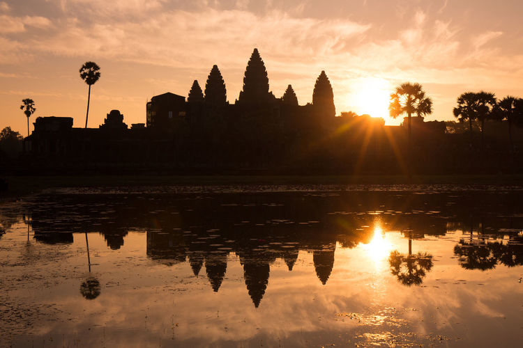 Silhouette temple by building against sky during sunset