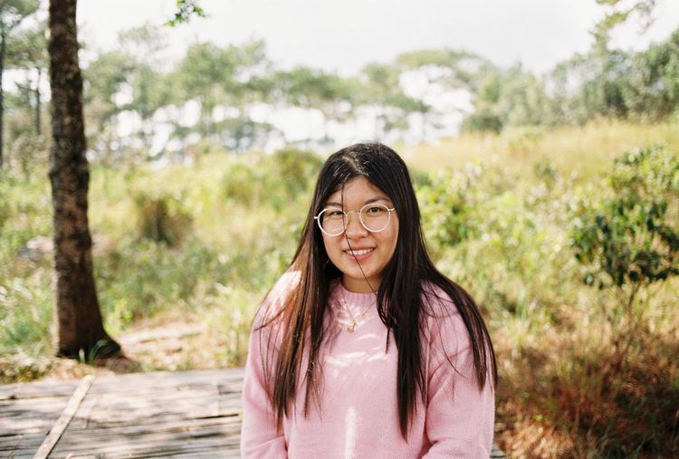 Portrait of young woman standing against trees