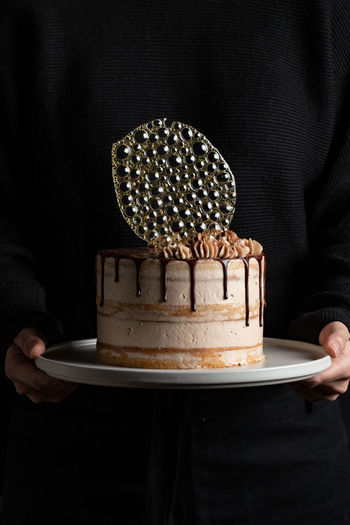 Unrecognizable person holding a festive cake with chocolate filling and frosting and silver isomalt decoration on table with black background