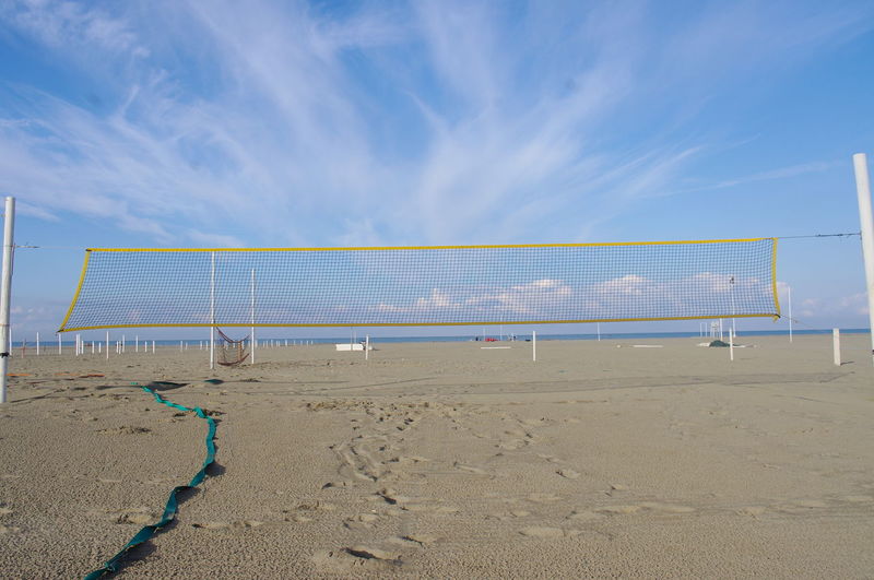 Net on sand at beach against blue sky