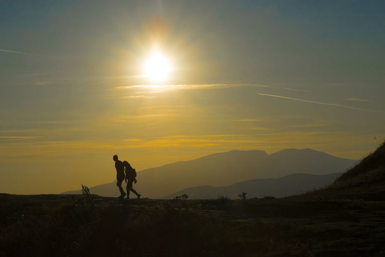 Silhouette couple walking on mountain during sunset