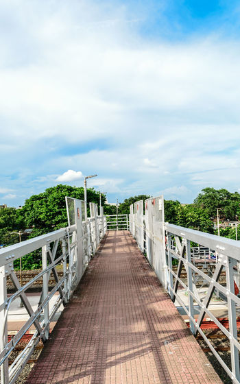 Empty footbridge along plants against sky
