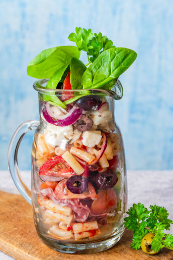 Salad with pasta, fresh vegetables, salami, olives and feta cheese in a jar - healthy lunch idea