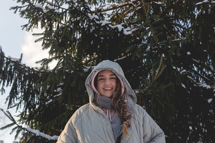 Woman with freckles in winter clothes outdoors enjoys winter, smiles and looks at the camera