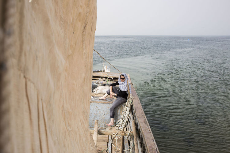 Woman sitting in fishing boat on sea against clear sky