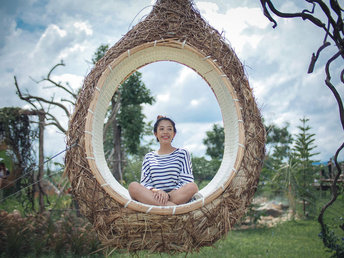 Smiling young woman sitting on swing against sky
