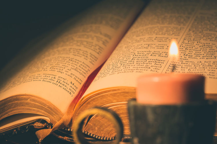 Close-up of lit candle and bible on table in darkroom