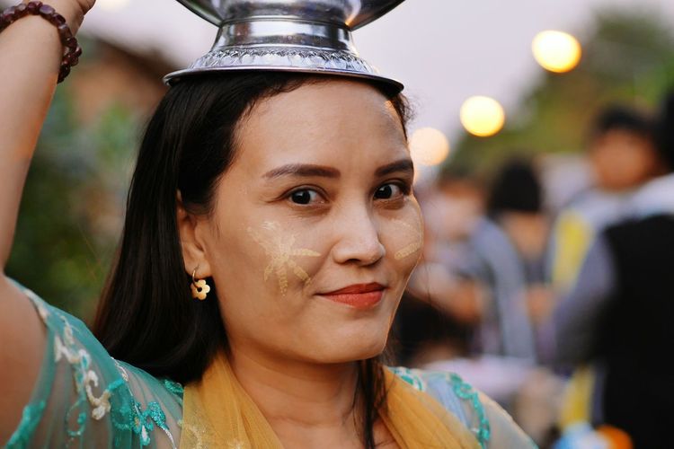Portrait of smiling woman with face paint carrying containers on head during event
