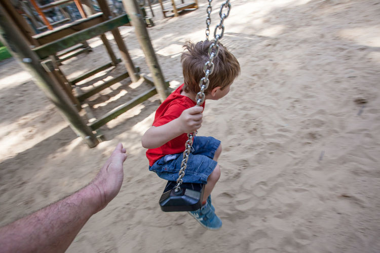 Cropped image of hand touching boy enjoying swing in park