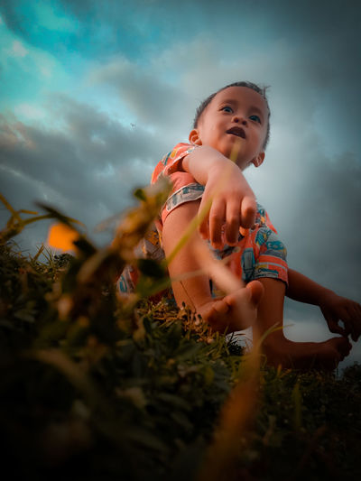 Low angle view of cute baby girl on field against sky