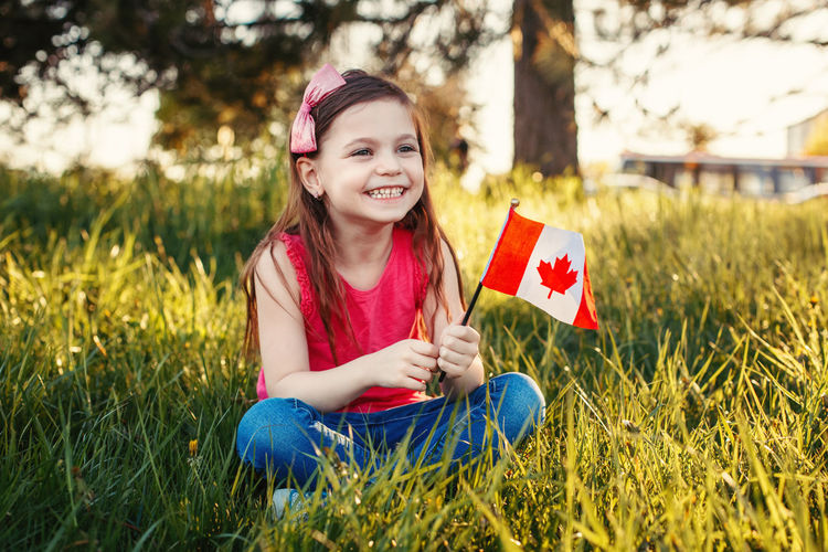 Happy girl with canadian flag sitting on field