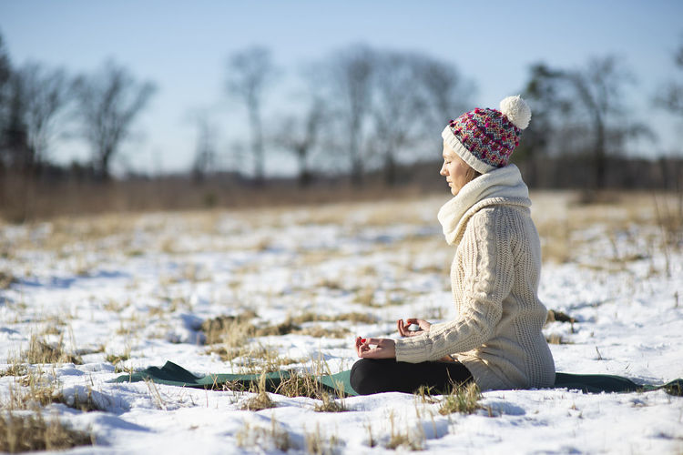 Young athletic woman sitting and meditatingin the yoga pose on snowy field during winter or spring