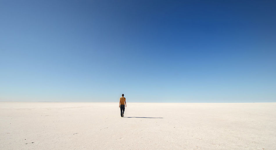 Full length rear view of shirtless man walking on lake mackay against clear blue sky