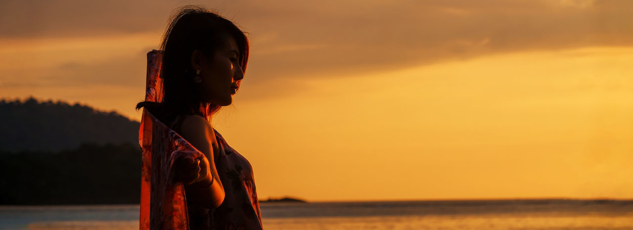 Silhouette of beautiful woman standing on beach at orange sunset on island in andaman sea