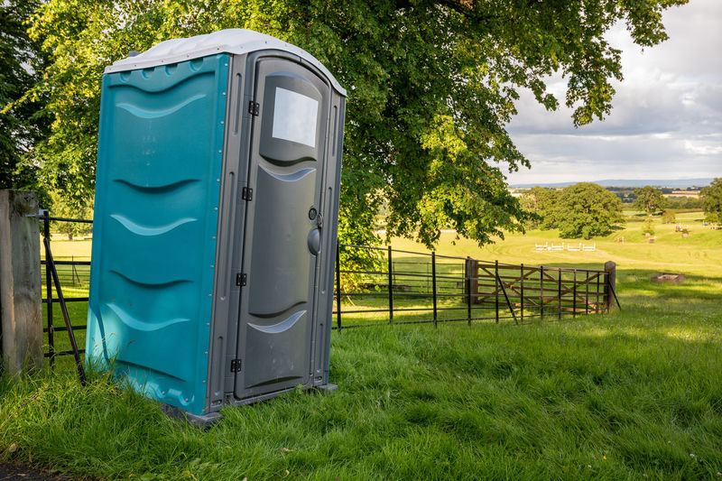 A plastic portable toilet in a field at an outdoor cross country horse trials event.