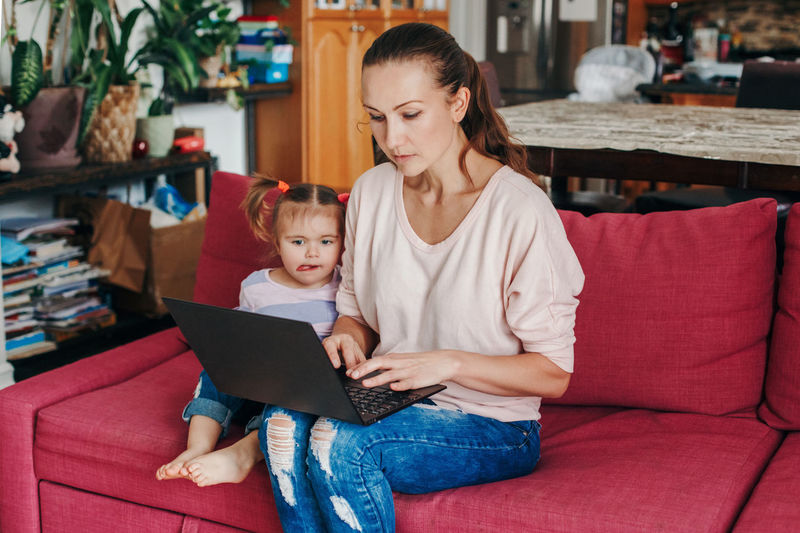 Caucasian mother with baby working on laptop from home. stay at home single at remote job online.