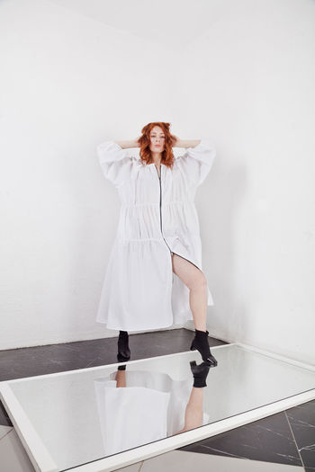 Authentic ginger fashion model posing indoors, white walls background, oversized dress clothes