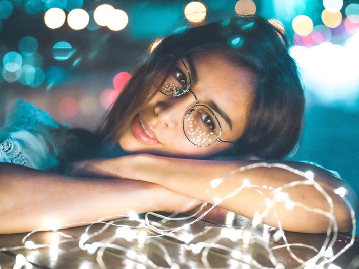 Smiling young woman with illuminated string lights lying on bed