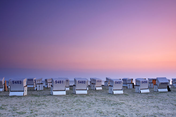 Hooded chairs on beach against clear sky at sunset