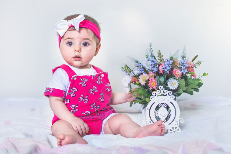 Portrait of cute baby girl with flowers sitting on bed at home