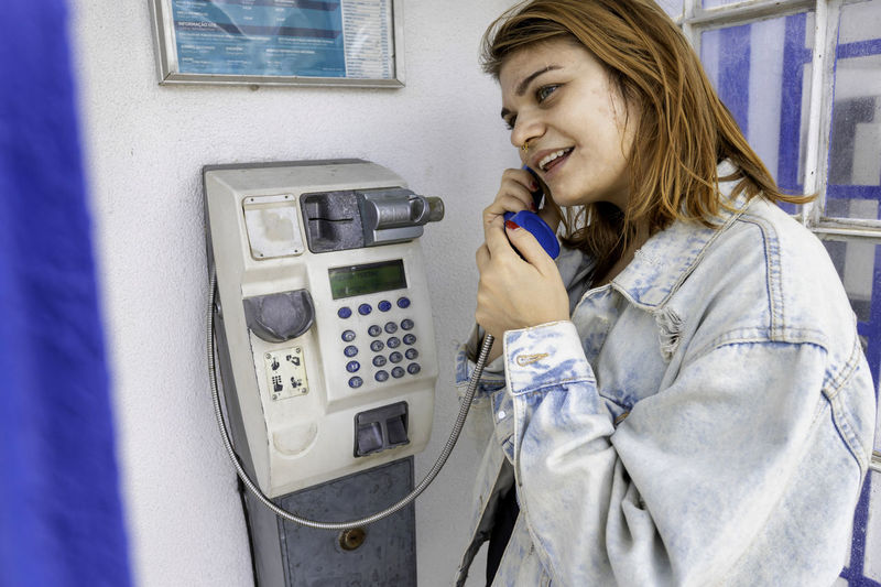 Cheerful woman using phone in telephone booth outdoors