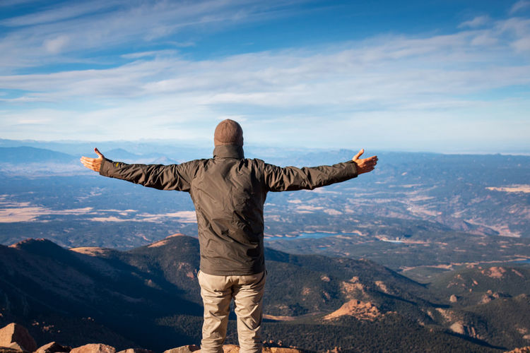 Rear view of man standing on top of pikes peak, colorado with arms wide open against sky