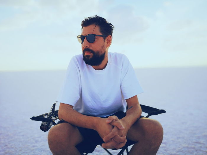 Young man sitting on chair against sea