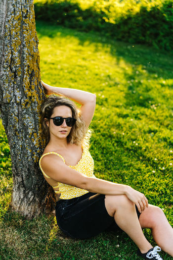 Young woman wearing sunglasses sitting on tree trunk
