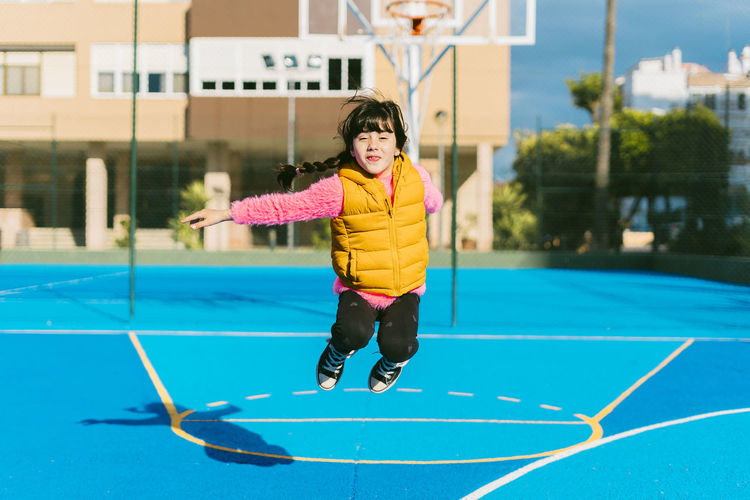 Cheerful girl jumping at sports court during sunny day