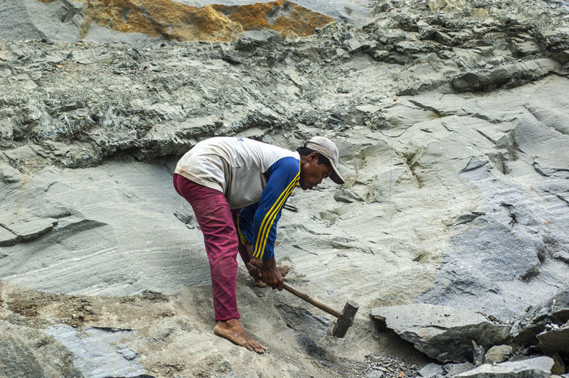 Side view of man hammering rock formations