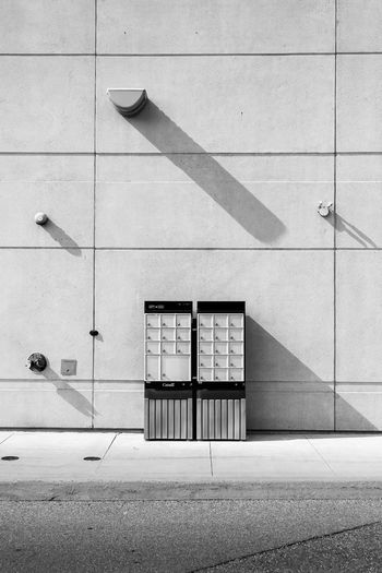 A black and white photograph of canadian mailboxes in a deserted big box retail shopping zone.
